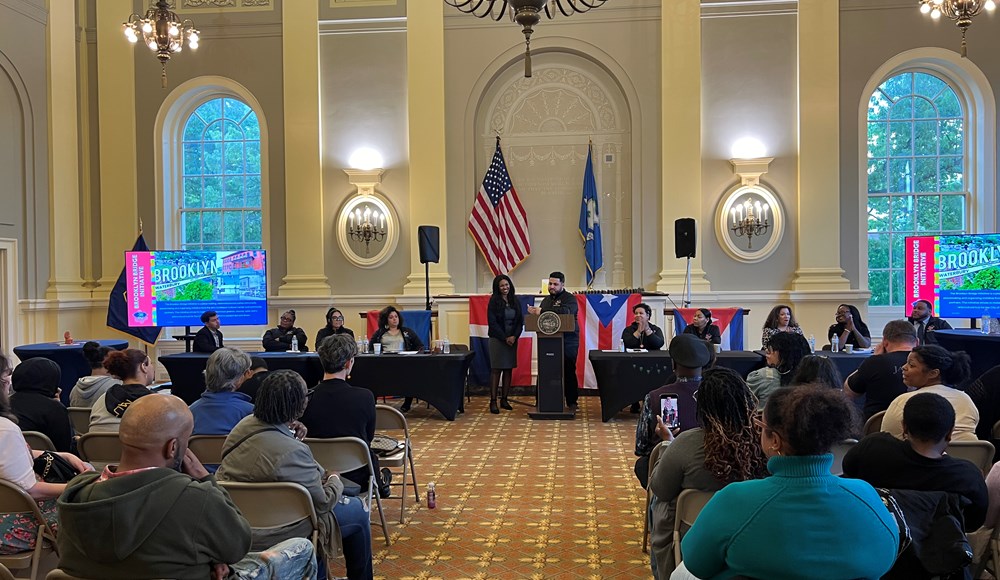 people at a podium and tables while audience listens