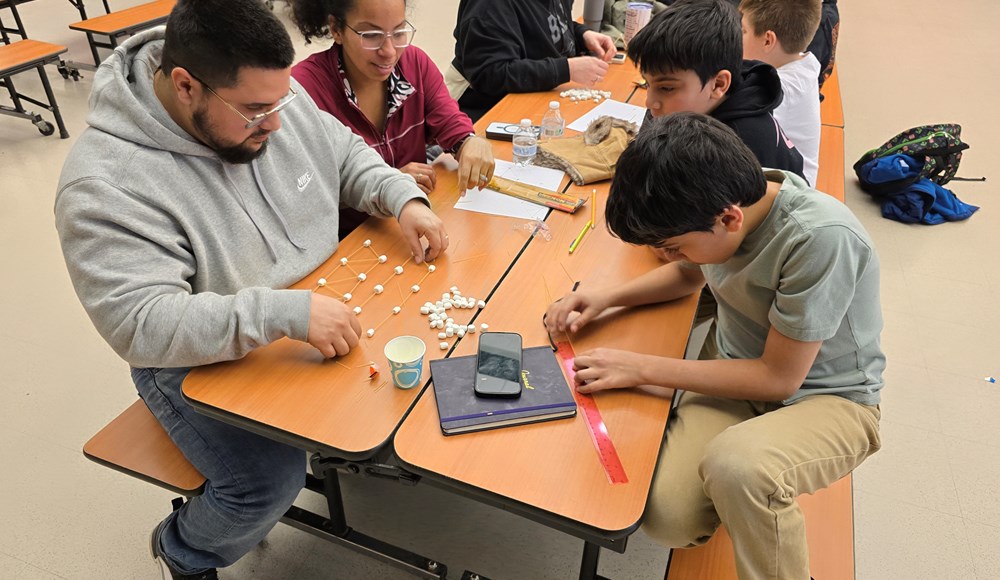 Adults and children making a bridge with spaghetti and marshmallows